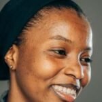 Close-up portrait of a smiling woman wearing a headscarf, exuding warmth and confidence.